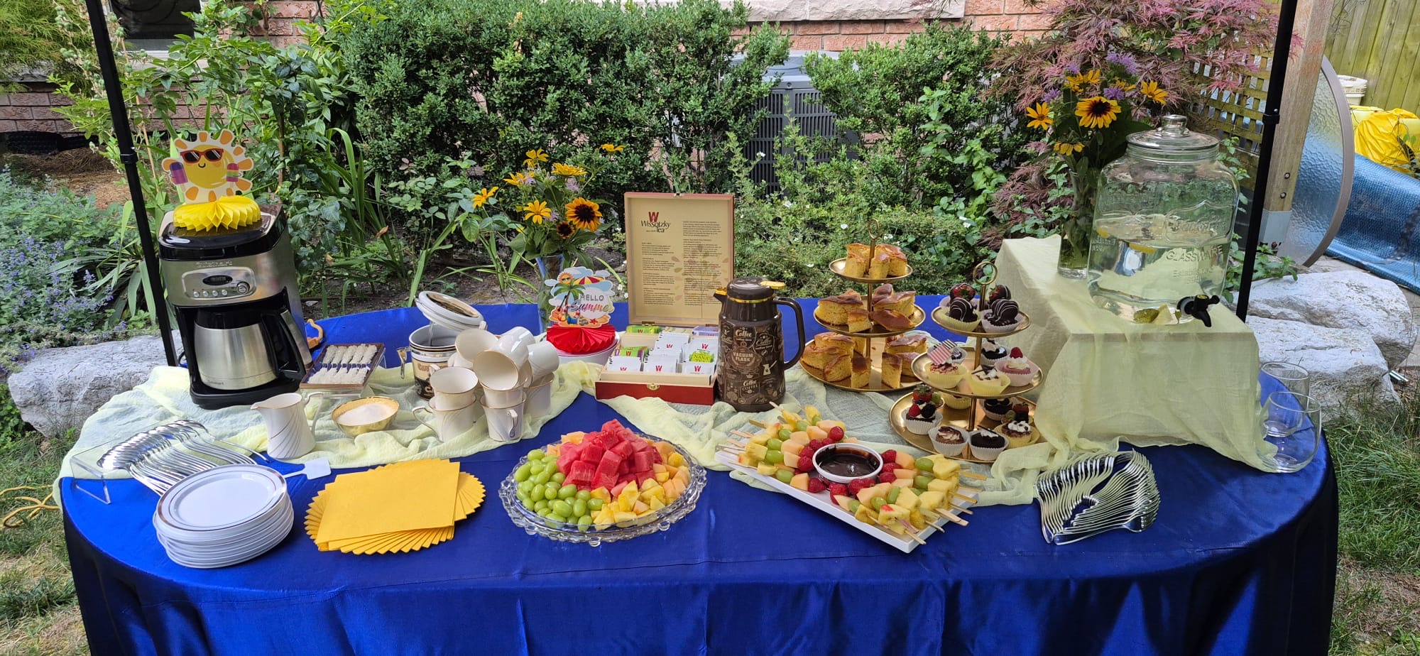 Outdoor garden catering table with fruit platters, pastries, and coffee station